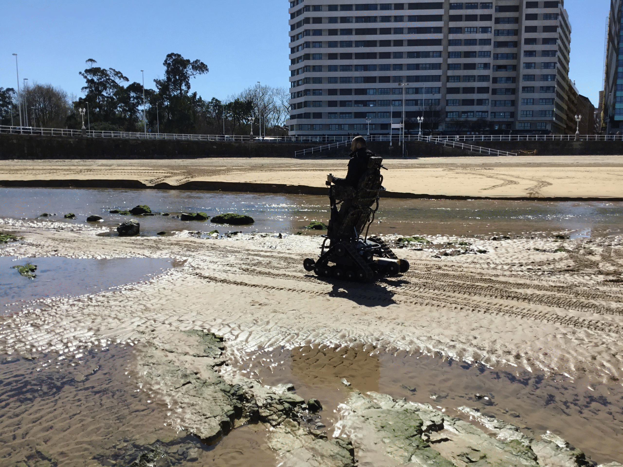 Persona en silla de ruedas todoterreno ontrack erguido en la playa cruzando un charco