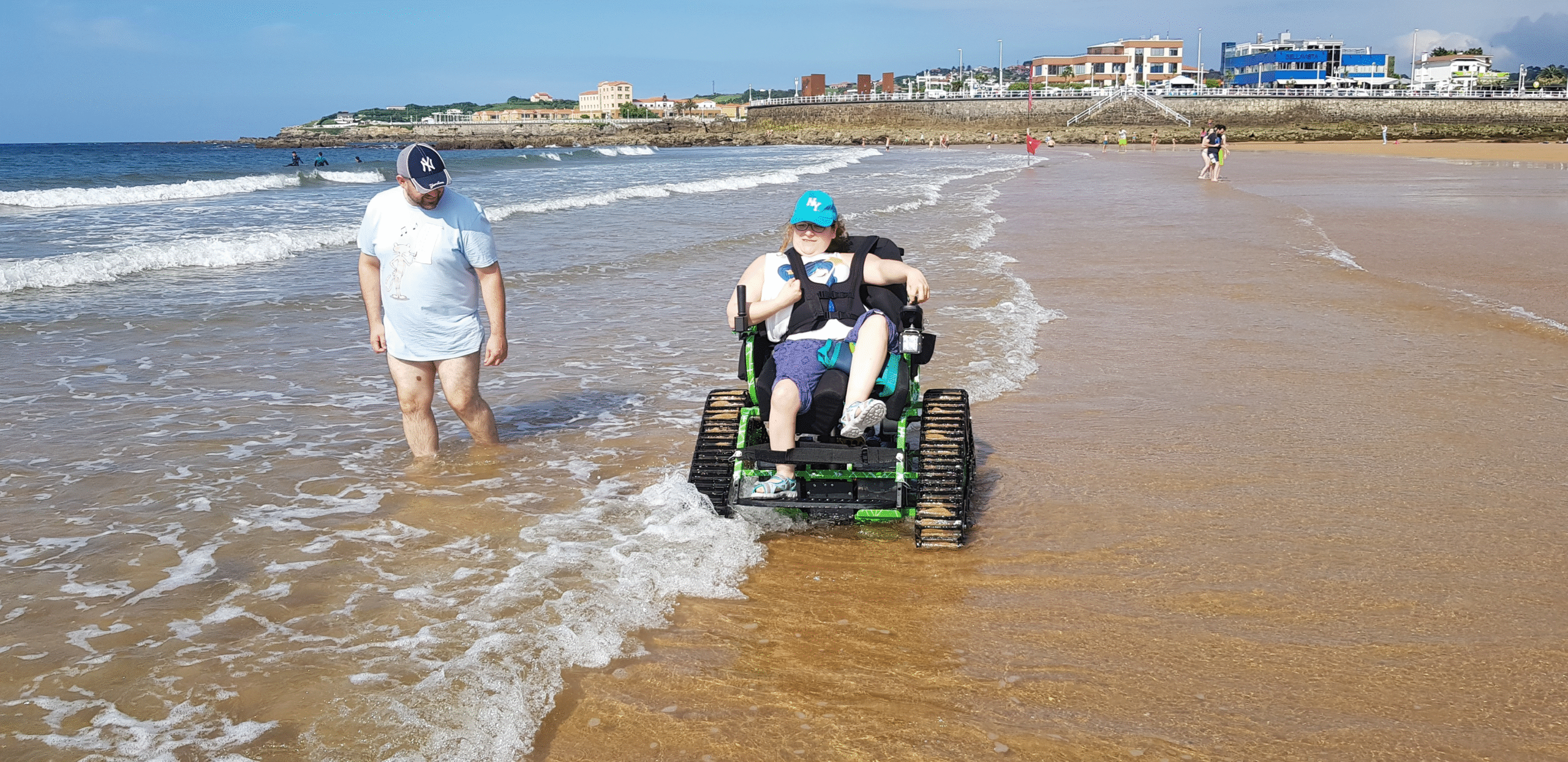 Persona en silla de ruedas todoterreno ontrack en la playa paseando junto a las olas