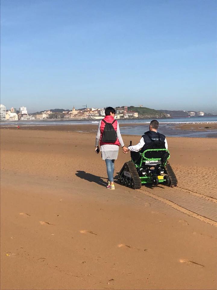 Persona en silla de ruedas todoterreno modelo ST caminando por la plata de la mano con otra persona